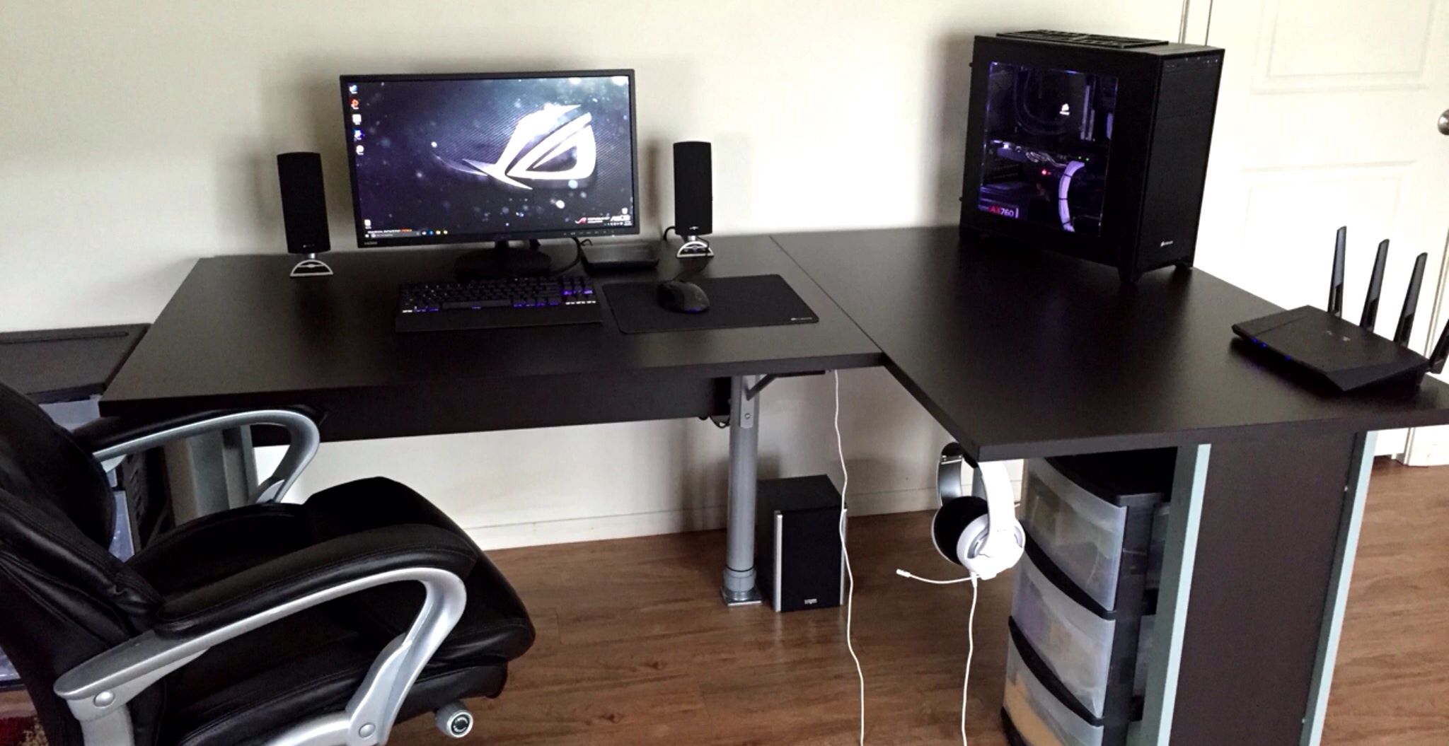 A gaming desk setup with monitor, mechanical keyboard, desk mat, and PC tower