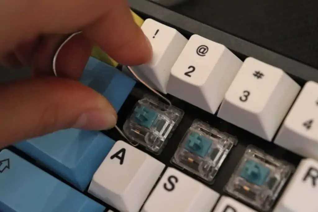 Removing a keycap to reveal exposed blue clicky switches on a hot-swappable mechanical keyboard